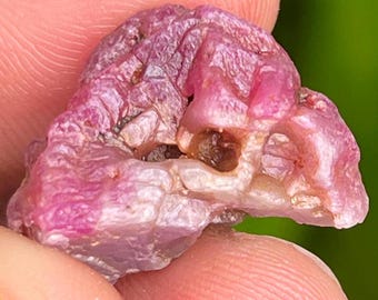 May include: A pink ruby crystal with a rough, natural texture. The crystal has a translucent appearance with a deep pink hue.