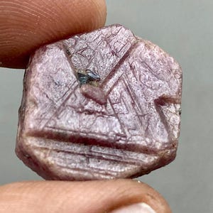 Op de afbeelding: Een diep roze robijnkristal met een gefacetteerde, geometrische vorm. Het kristal heeft een ruw, getextureerd oppervlak en is een natuurlijke edelsteen.