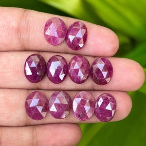 May include: Ten oval-cut rubies, each with multiple facets, creating a sparkling effect. The gemstones are a deep red hue. The rubies are displayed against a neutral background.
