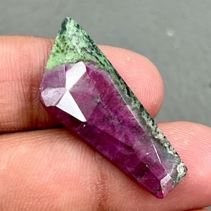 Può includere: Una pietra preziosa verde e rosa con taglio sfaccettato. La pietra preziosa ha una forma grezza e naturale e ha una punta appuntita.