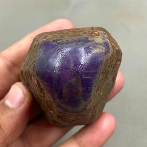 May include: A natural, uncut gemstone with a striking purple centre and a brown exterior. The stone has an irregular shape and a polished, reflective surface. This is a natural mineral specimen, perfect for collectors.