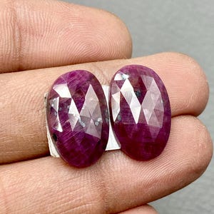Puede incluir: Dos piedras preciosas de rubí talladas en forma ovalada, de color rojo intenso. Las piedras preciosas están engastadas en plata.