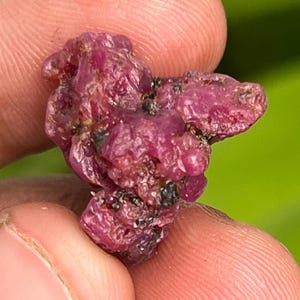 Puede incluir: Un grupo de cristales de rubí en bruto de color rosa intenso. Los cristales son ásperos y tienen un aspecto natural sin pulir.