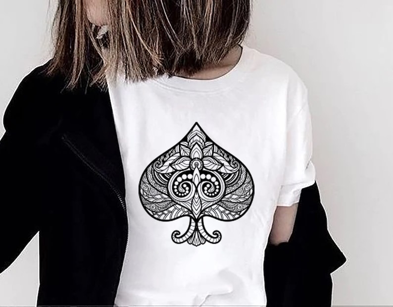 May include: A white t-shirt with a black and white graphic of a spade playing card. The spade is intricately designed with a floral pattern.
