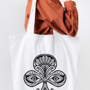 May include: A white tote bag with a black and white illustration of a stylized clover with eyes. The clover is a common symbol for good luck.