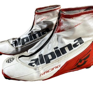 Puede incluir: Par de botas de esquí de carreras Alpine blancas y rojas. Las botas tienen cierre de cremallera y la palabra "Alpine" está impresa en letras negras grandes. La palabra "Racing" está impresa en rojo.
