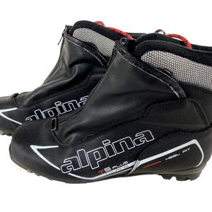 May include: Pair of black Alpina TS Plus cross-country ski boots. The boots have a zippered front, white and red accents, and the brand name in white. The boots have a mesh collar and red laces.