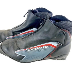 Puede incluir: Par de botas de esquí de fondo Salomon Escape 5 TR negras. Las botas tienen una cremallera frontal, detalles en gris y rojo, y el logotipo de Salomon. Diseñadas para deportes de invierno y actividades al aire libre.