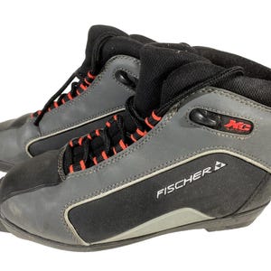 Puede incluir: Par de botas de esquí de fondo Fischer XC grises y negras. Las botas tienen cordones negros con detalles rojos, un cuello acolchado negro y el logotipo de Fischer. Diseñadas para deportes de invierno.