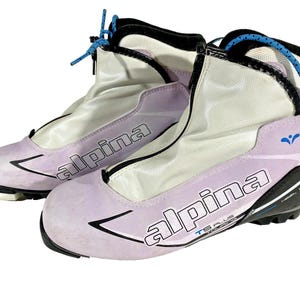 Peut inclure: Paire de chaussures de ski Alpina TS Plus lavande et blanches. Les chaussures ont des détails noirs, des lacets bleus et le logo Alpina en noir. Ces chaussures de ski sont conçues pour le ski et ont une conception montante pour le maintien de la cheville.