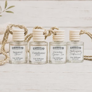 May include: Four clear glass car diffuser bottles with wooden caps and hanging ropes. Each bottle features a white label with the Farmstead Candle Co. logo, scent name, and Net Wt. 18ml. Scents include Sugared Lemon, Farmhouse Pear, Cucumber Green Tea, and Mahogany Teakwood.