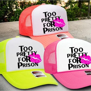 May include: Three trucker hats in neon colors: yellow, pink, and orange. Each hat has a white front panel with the text "Too Pretty For Prison" and a pink lip graphic. The hats have mesh backs and curved brims.