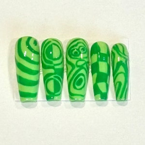 May include: Set of six green and white patterned false nails. The nails have different geometric designs, including stripes, swirls, and checkerboard patterns.