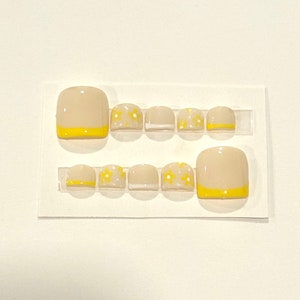 May include: A set of 10 beige toe nail wraps with a yellow accent and a white daisy design.