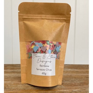May include: A brown paper bag with a clear window showing colorful terrazzo chips. The bag has a label that reads "Stem & Stone Designs, Rainbow Terrazzo Chips, 60g".