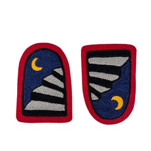 May include: Two embroidered patches with a night sky theme. Each patch has a red border, a dark blue background, and a crescent moon. One patch features a staircase design, and the other has a mountain-like design.