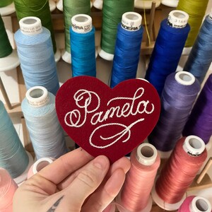 hand holding red custom felt heart patch with the "Pamela" embroidered in fancy cursive script