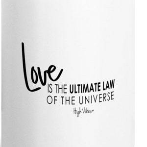 May include: White ceramic coffee mug with black text that reads "Love is the ultimate law of the universe - High Vibes"
