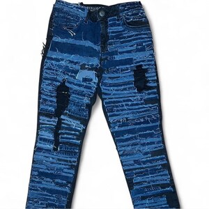 Könnte beinhalten: Blaue Jeans aus Denim mit mehreren Schichten aus Denim, die zusammengenäht wurden, um einen Patchwork-Effekt zu erzeugen. Die Jeans haben mehrere abgenutzte Stellen und sind an einigen Stellen zerrissen.