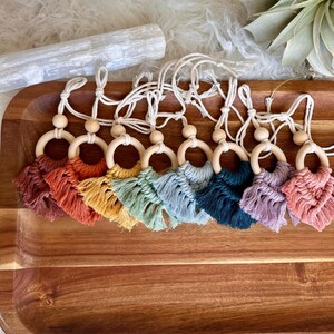 May include: A set of eight wooden ring and tassel baby toys in various colors, including red, orange, yellow, green, blue, teal, purple, and pink. The toys are strung on a white cord and are arranged in a rainbow pattern.