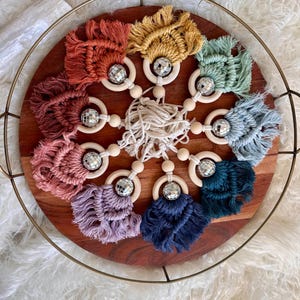 以下が含まれることがあります： カラフルなクロシェのタッセルとシルバーのディスコボールのアクセントが付いた、木製ベビーラトル8個セット。ラトルは木製のトレイに円形に配置されています。