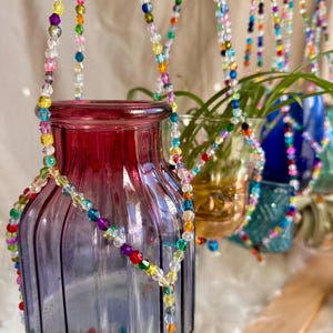 May include: A set of glass vases with colorful beaded hangers. The vases are clear and have a textured surface. The beads are multi-colored and create a rainbow effect.
