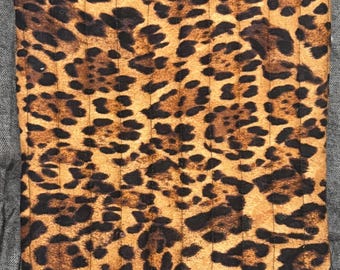 May include: A rectangular, quilted pouch with a leopard print pattern in shades of brown and black. The pouch has a black zipper closure and a small white label with black text that reads "KCD Apparel & Accessories."