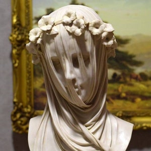 Puede incluir: Busto de mujer en mármol blanco con un velo drapeado y una corona de flores. El busto está sobre un pedestal blanco.