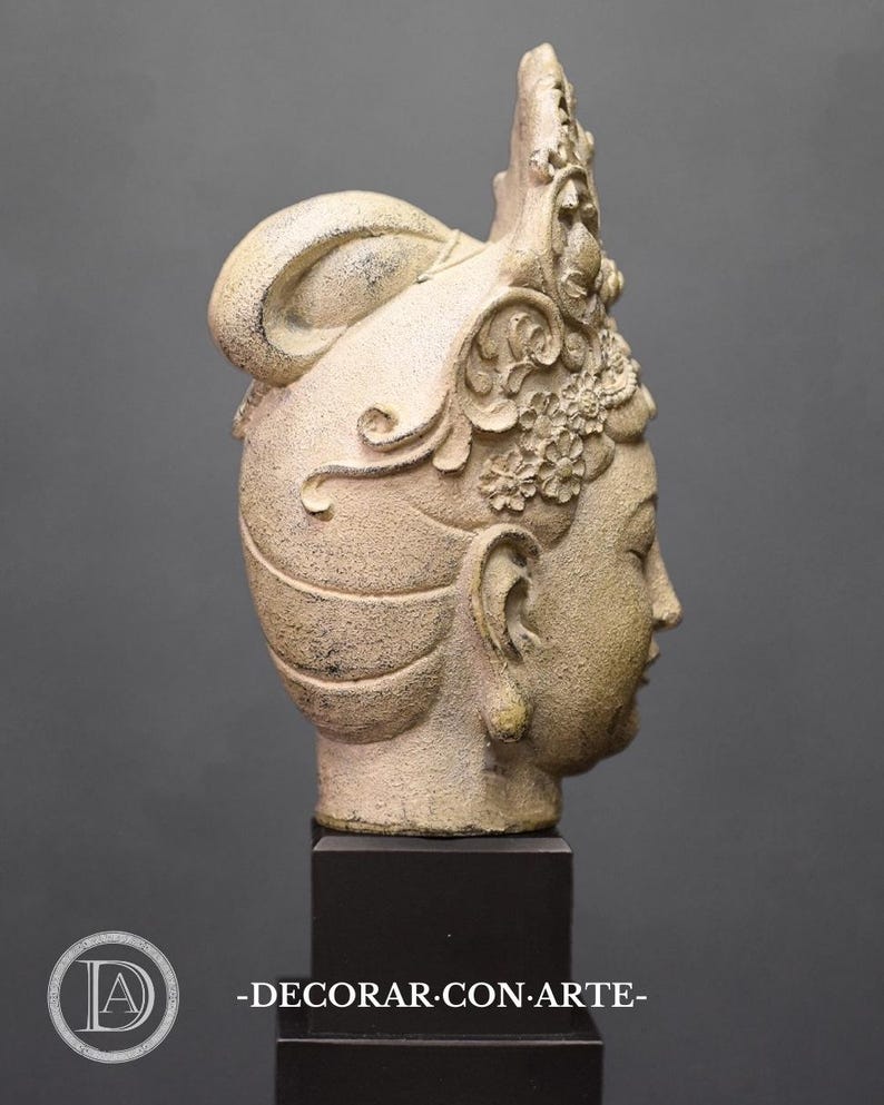 May include: A white ceramic sculpture of a woman's head with a detailed crown and elaborate hairstyle. The sculpture is on a black pedestal.