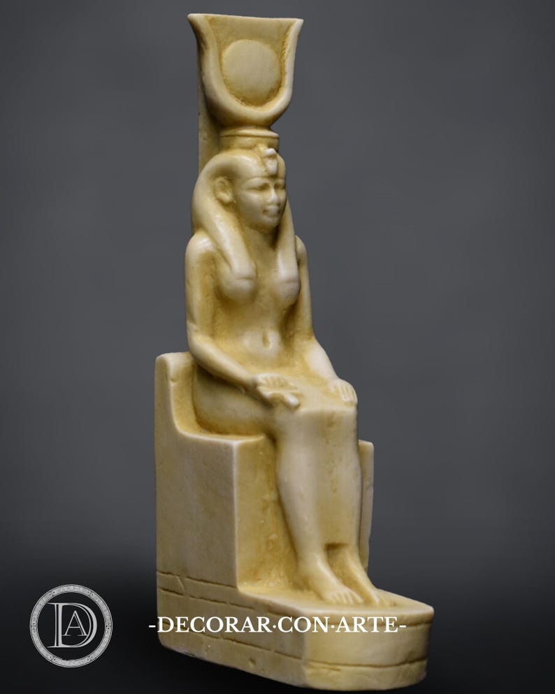 Puede incluir: Una escultura de piedra blanca de una diosa egipcia sentada en un trono. La diosa lleva una corona y una larga t&uacute;nica fluida. La escultura mide aproximadamente 25 cm de alto.