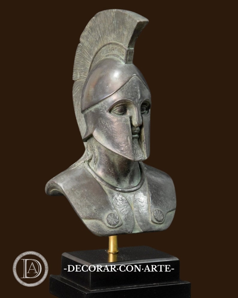 May include: A bronze-colored bust of a warrior wearing a helmet with a tall crest. The bust is mounted on a black rectangular base. The warrior's armor includes shoulder decorations. The bust is a decorative item.