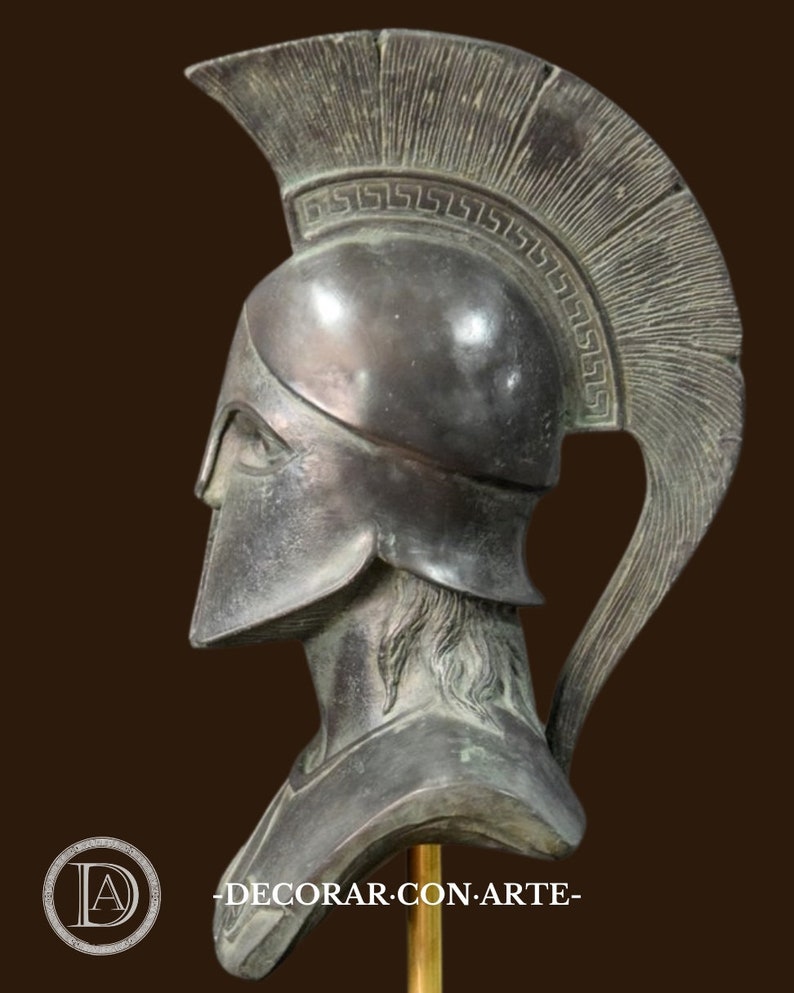 May include: A bronze-colored bust of a Spartan warrior, featuring a detailed helmet with a crest and a decorative border. The bust is mounted on a gold-colored stand, with the text "DECORAR.CON.ARTE" visible.