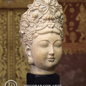 May include: A beige stone sculpture of a woman's head with a detailed crown and closed eyes. The sculpture is on a black base.