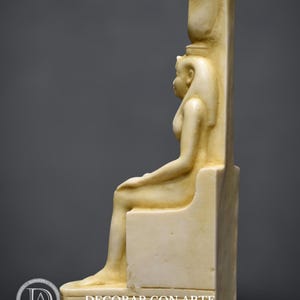 Puede incluir: Una estatua blanca sentada de una diosa egipcia con un alto tocado. La estatua est&aacute; hecha de un material liso y pulido y est&aacute; sentada en un trono. La diosa lleva una larga t&uacute;nica fluida y tiene una expresi&oacute;n serena en su rostro.
