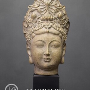 May include: A beige stone sculpture of a Buddha head with closed eyes and a crown of intricate floral designs. The sculpture is mounted on a black base.