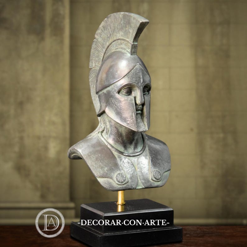 May include: A bronze-toned bust of a classical warrior, complete with a helmet and chest armor. The sculpture is mounted on a black rectangular base. The text "-DECORAR-CON-ARTE-" is visible on the base.
