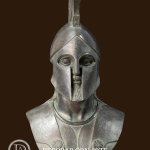 May include: A bronze-colored bust of a Spartan warrior, complete with a helmet and chest armor. The bust features a detailed face and beard, with the text "DECORAR CON ARTE" visible in the lower portion of the image.