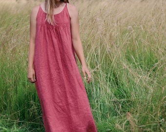 Puede incluir: Una mujer con un vestido largo de lino rojo se encuentra en un campo de hierba alta.