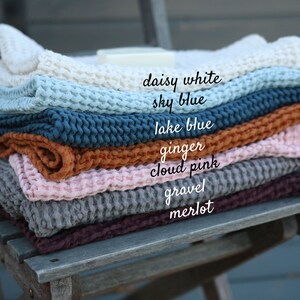May include: A stack of waffle weave cotton throws in various colours, including daisy white, sky blue, lake blue, ginger, cloud pink, gravel, and merlot.
