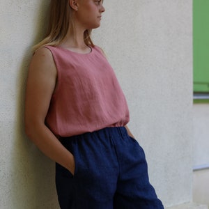 May include: A woman wearing a sleeveless, blush-colored linen top with a navy blue linen pair of pants.