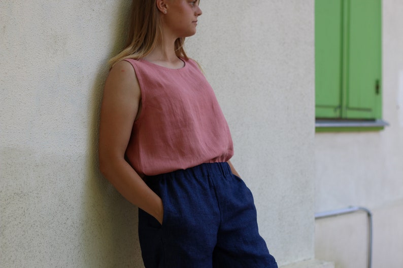 May include: A woman wearing a sleeveless, blush-colored linen top with a navy blue linen pair of pants.