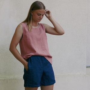 May include: A woman wearing a sleeveless, dusty rose linen top and dark blue linen shorts. The top has a scoop neck and the shorts have a cuffed hem.