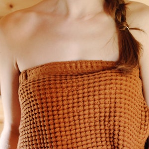 May include: A close-up of a person wearing a brown waffle weave towel wrapped around their chest. The towel is textured and has a waffle pattern.