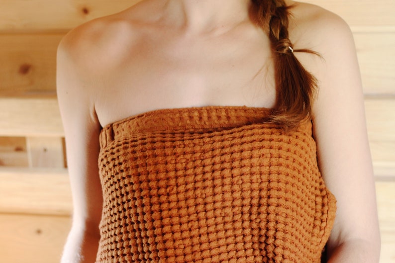 May include: A close-up of a person wearing a brown waffle weave towel wrapped around their chest. The towel is textured and has a waffle pattern.