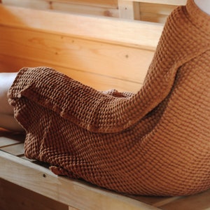 May include: A person relaxing on a wooden bench in a sauna, wrapped in a brown waffle weave towel.