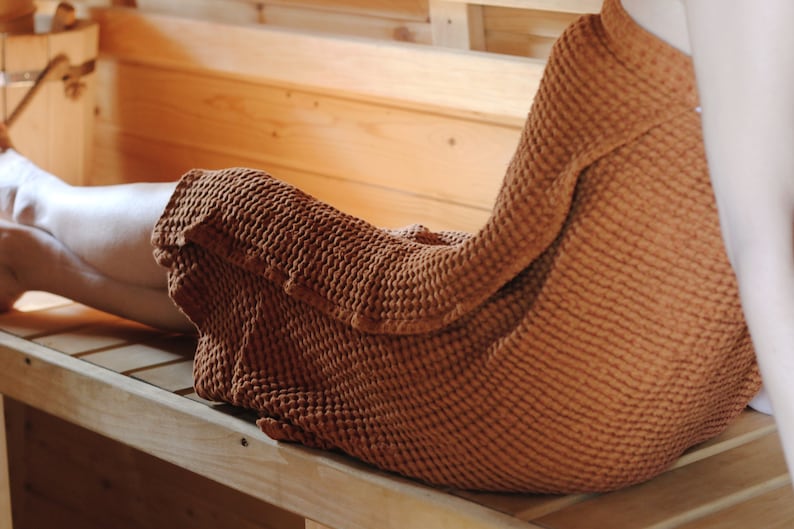 May include: A person relaxing on a wooden bench in a sauna, wrapped in a brown waffle weave towel.