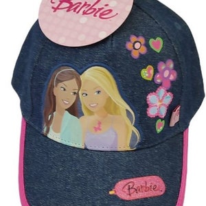 Könnte beinhalten: Eine blaue Jeans-Baseballkappe mit rosafarbenem Schirm und einem rosafarbenen Etikett mit der Aufschrift "Barbie". Die Vorderseite der Kappe zeigt eine bunte Grafik mit zwei Barbie-Puppen, Blumen und Herzen.