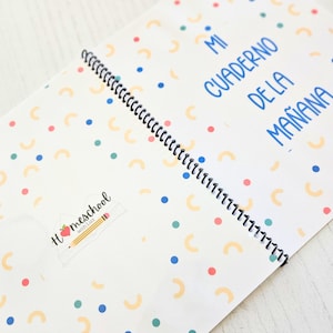 May include: A spiral-bound notebook with a white cover featuring a pattern of small blue and teal dots and yellow semi-circles. The text "MI CUADERNO DE LA MA&Ntilde;ANA" is printed in blue, and a logo with a pencil and apple reads "Homeschool with Lizz".