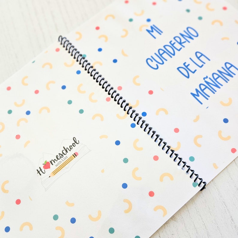 May include: A spiral-bound notebook with a white cover featuring a pattern of small blue and teal dots and yellow semi-circles. The text "MI CUADERNO DE LA MA&Ntilde;ANA" is printed in blue, and a logo with a pencil and apple reads "Homeschool with Lizz".