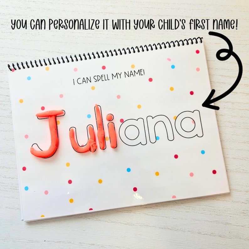 May include: A white book with a colorful confetti pattern and the text "I can spell my name!"  The name "Juliana" is written in black outline and filled in with pink playdough.
